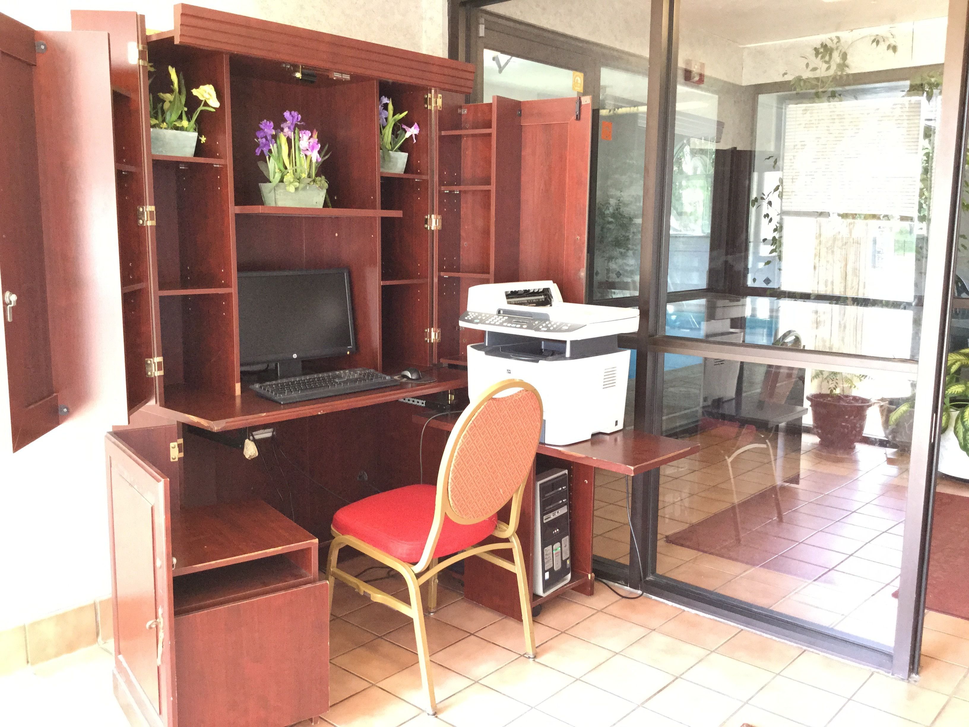 Um espaço de escritório compacto com escrivaninha, cadeira, computador, impressora e prateleiras com plantas.