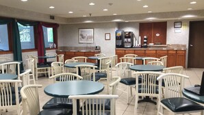 A dining area with round tables and white chairs, a kitchen counter with appliances, and a framed picture on the wall.
