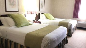 Habitación de hotel con dos camas, cada una con ropa de cama verde y blanca, una mesita de noche con teléfono y control remoto, y cuadros con motivos florales en las paredes.
