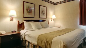 A hotel room with a large bed, two bedside lamps, a nightstand with a phone and alarm clock, and two framed floral pictures on the wall.