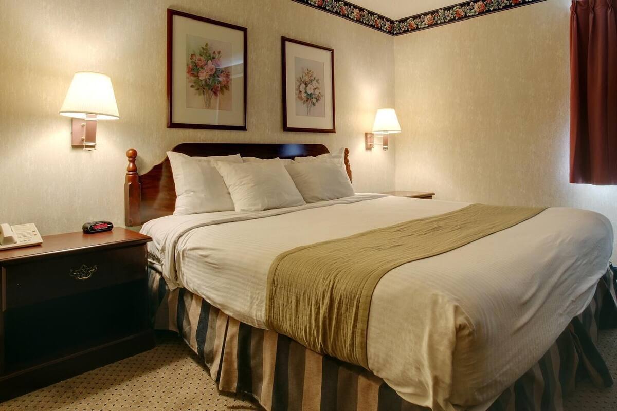 A hotel room with a large bed, two bedside lamps, a nightstand with a phone and alarm clock, and two framed floral pictures on the wall.