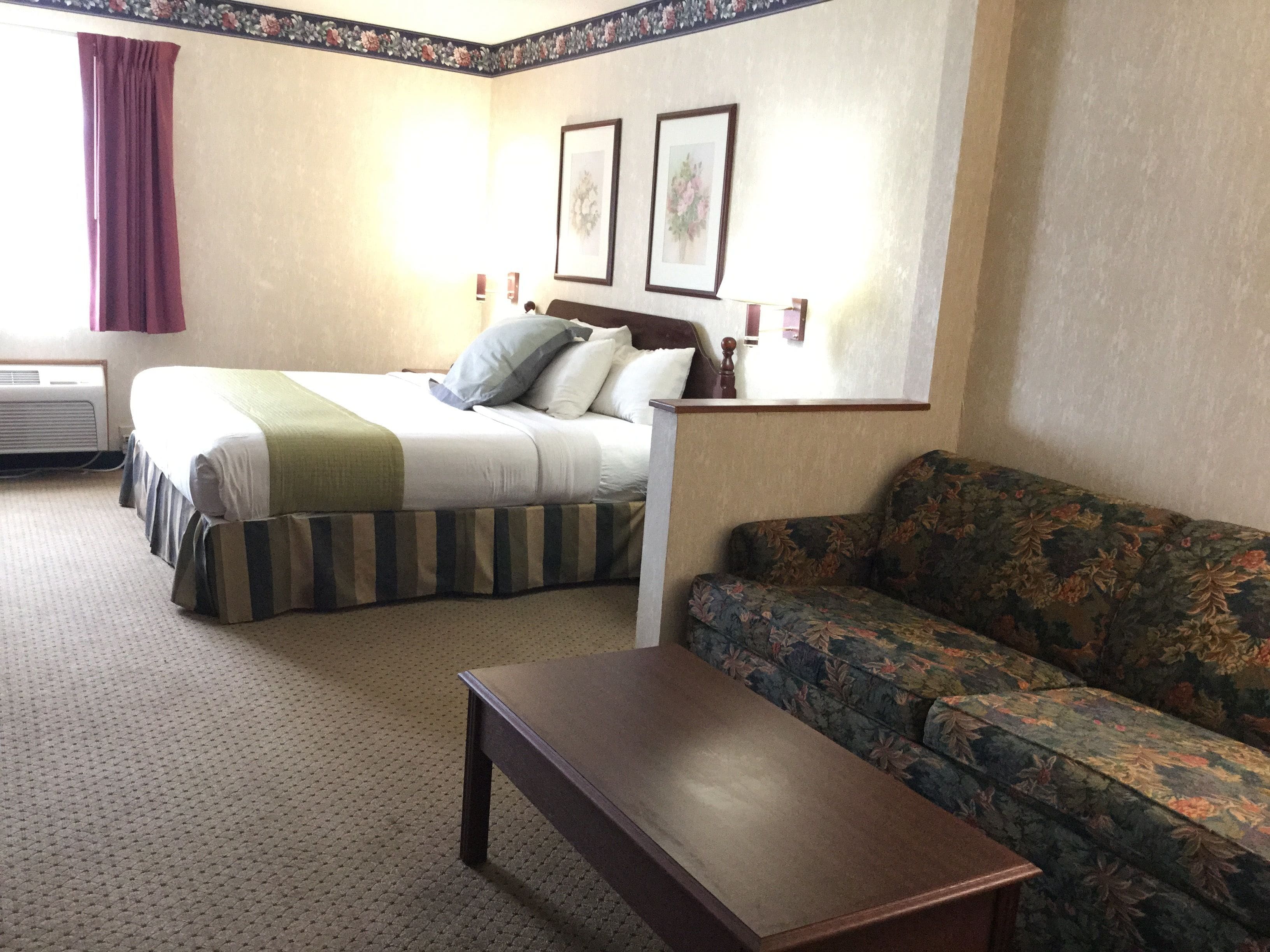 Una habitación de hotel con una cama, un sofá, una mesa y dos cuadros en la pared.