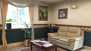 A living room with a beige sofa, a wooden coffee table, a patterned rug, a potted plant, and two framed pictures on the wall.