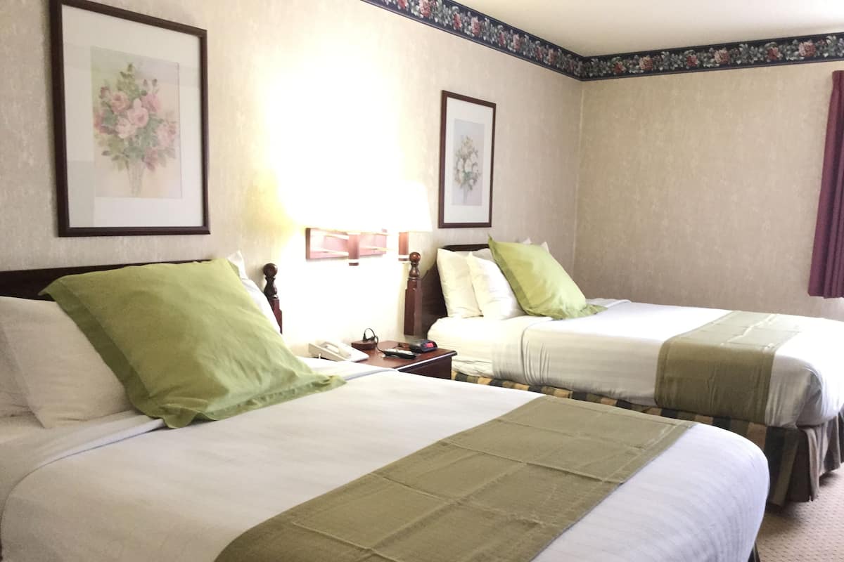 A hotel room with two beds, each with a green throw blanket, white bedding, and a nightstand with a telephone and lamp.
