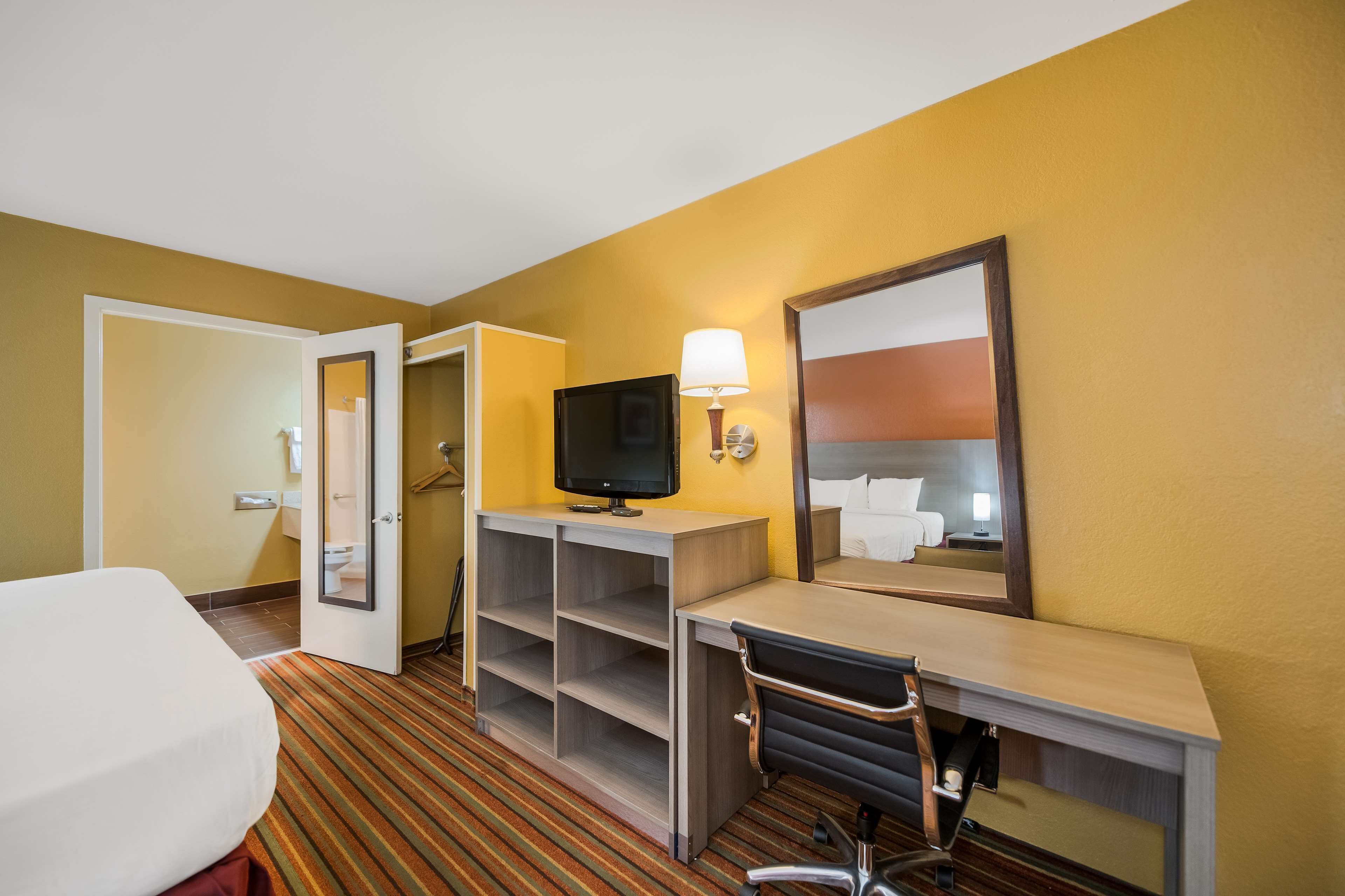 Una camera d'albergo con un letto, una scrivania, una TV e uno specchio.