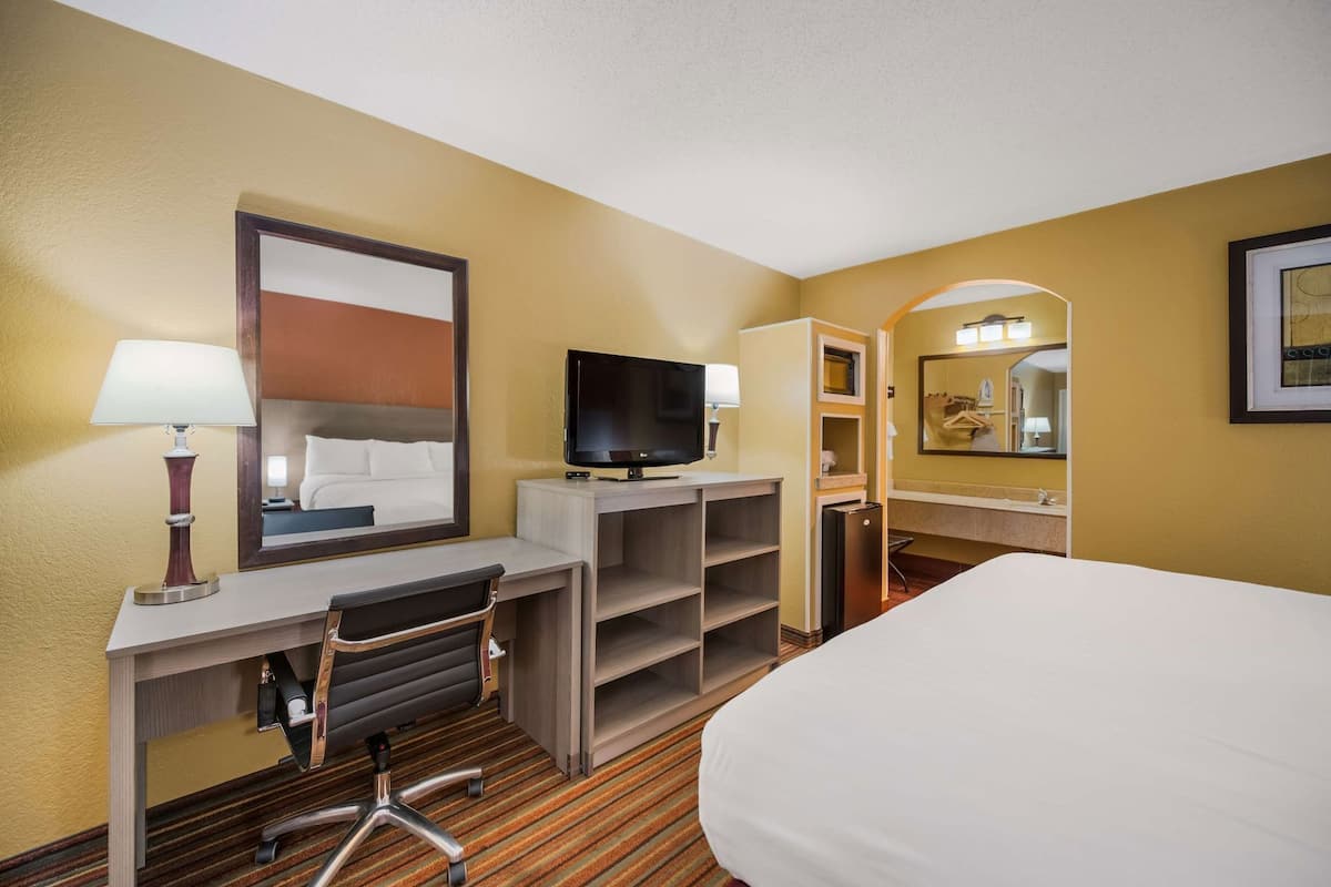A hotel room with a bed, desk, chair, TV, and a mirror.