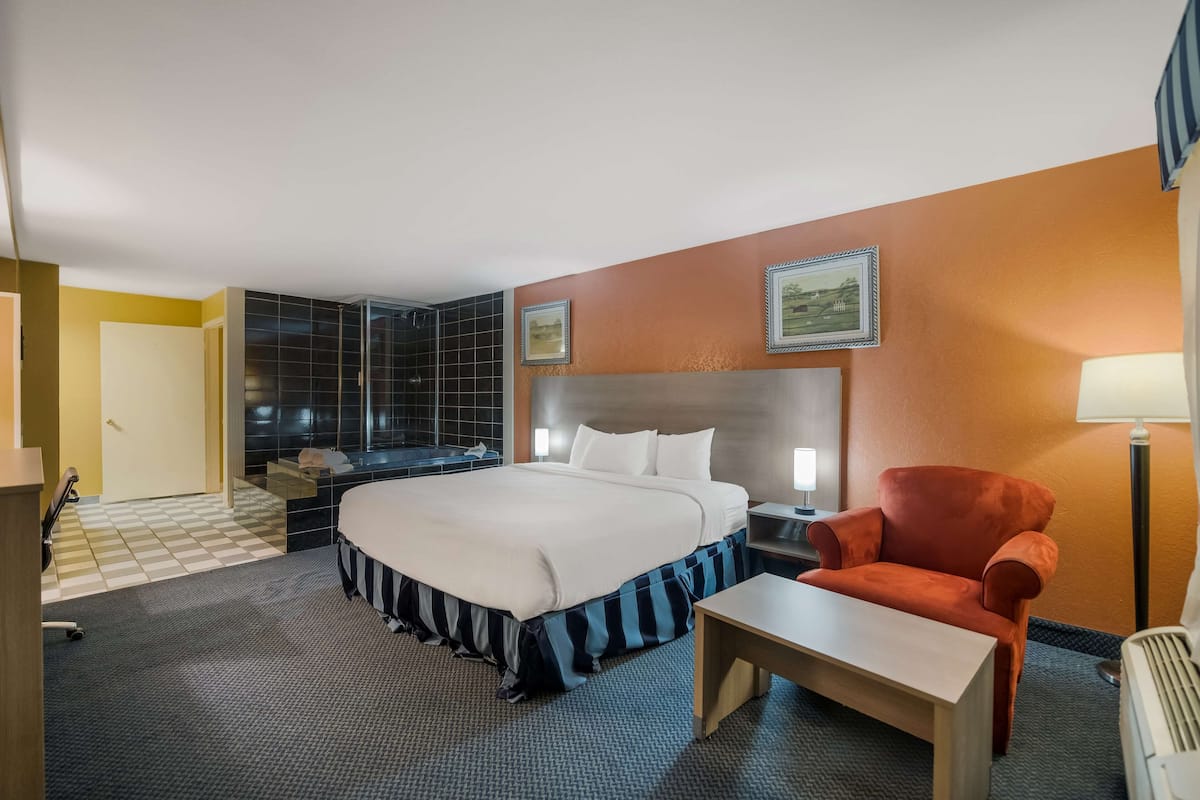 A hotel room with a large bed, a desk, a chair, a nightstand, a lamp, and a picture on the wall.