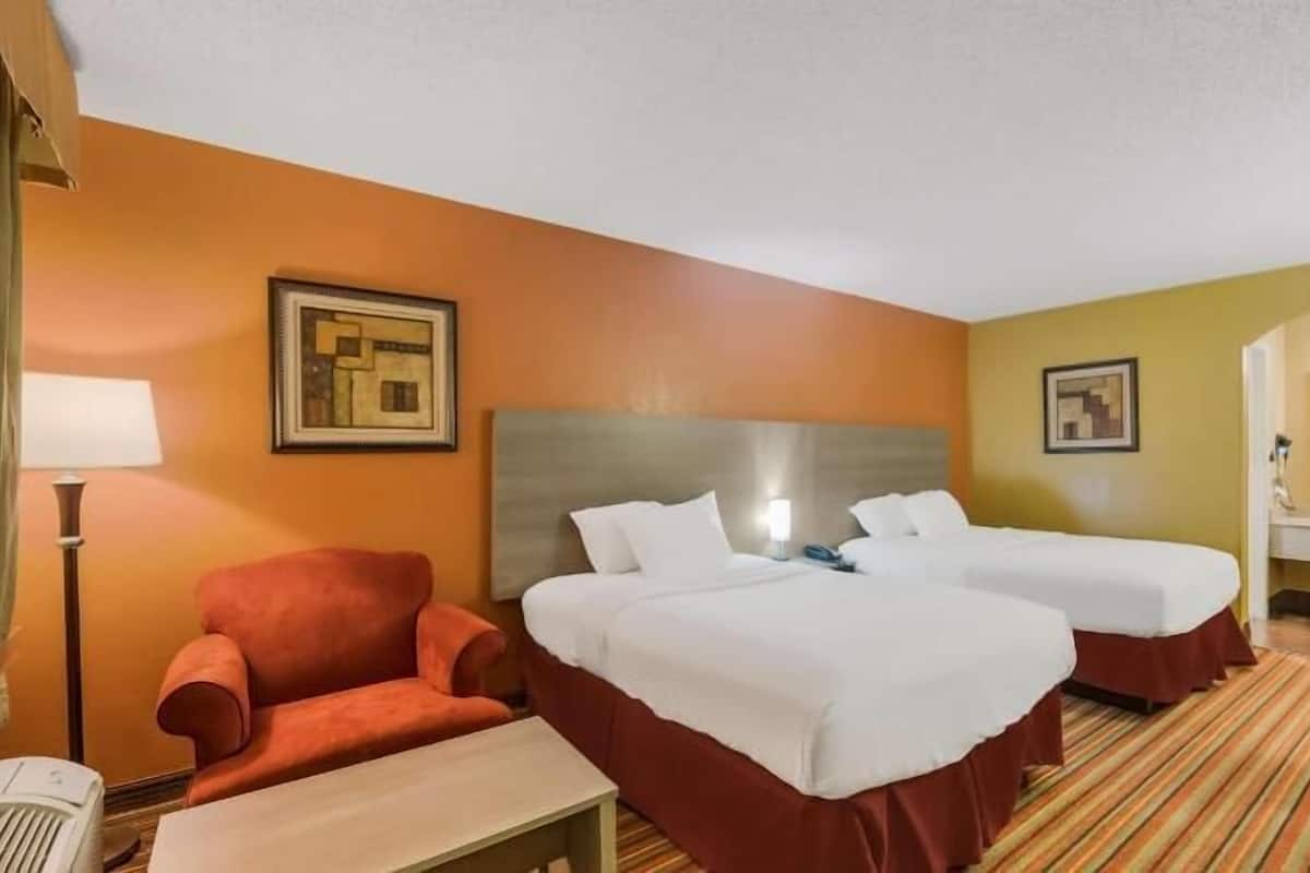 A hotel room with two beds, a desk, a chair, a lamp, and artwork on the walls.