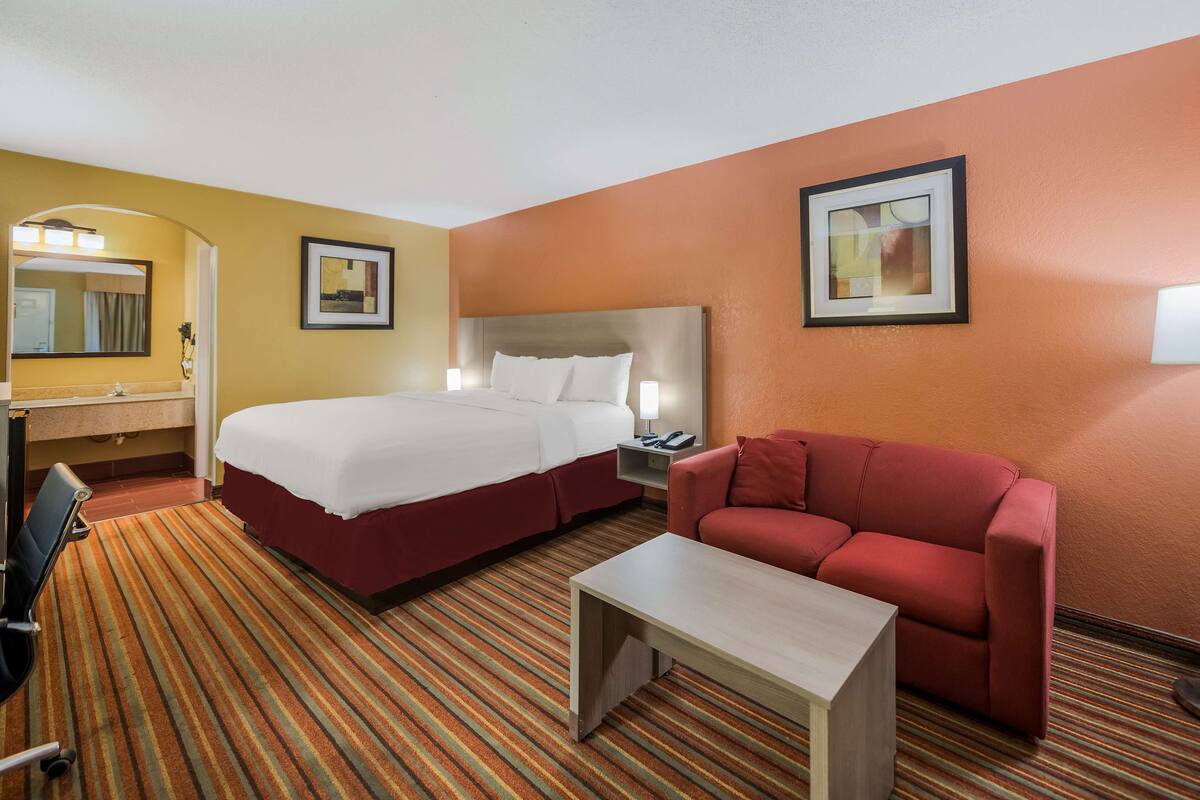 A hotel room with a bed, a red sofa, a small table, a desk, a chair, and a mirror.