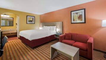 A hotel room with a bed, a red sofa, a small table, a desk, a chair, and a mirror.