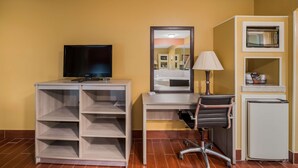 A room with a desk, chair, television, lamp, and a small refrigerator.