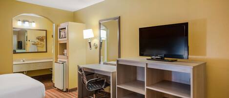 Quarto de hotel com duas camas, uma escrivaninha, uma cadeira, uma televisão, um espelho e uma estante.