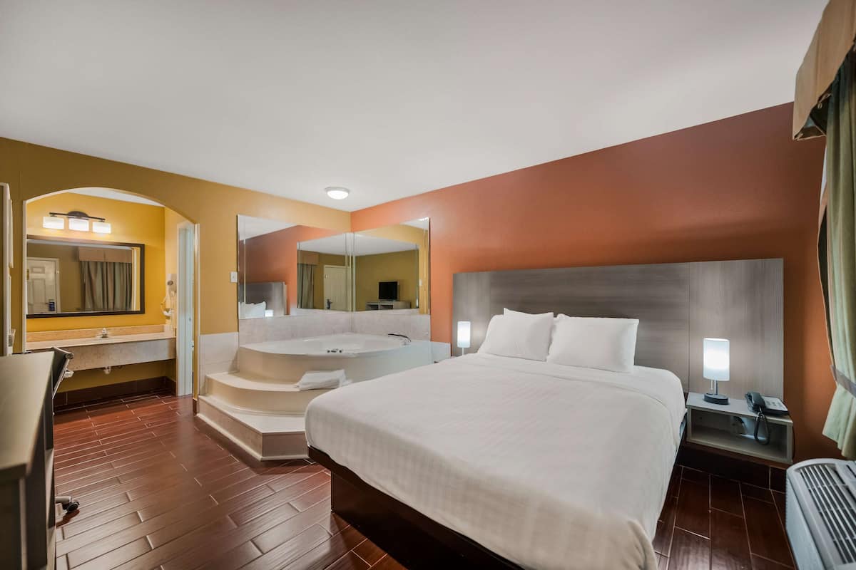 A hotel room with a large bed, a bathroom with a bathtub, a desk, and a chair.