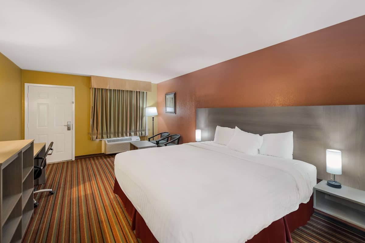 A hotel room with a large bed, a desk, a chair, a lamp, and a window with curtains.