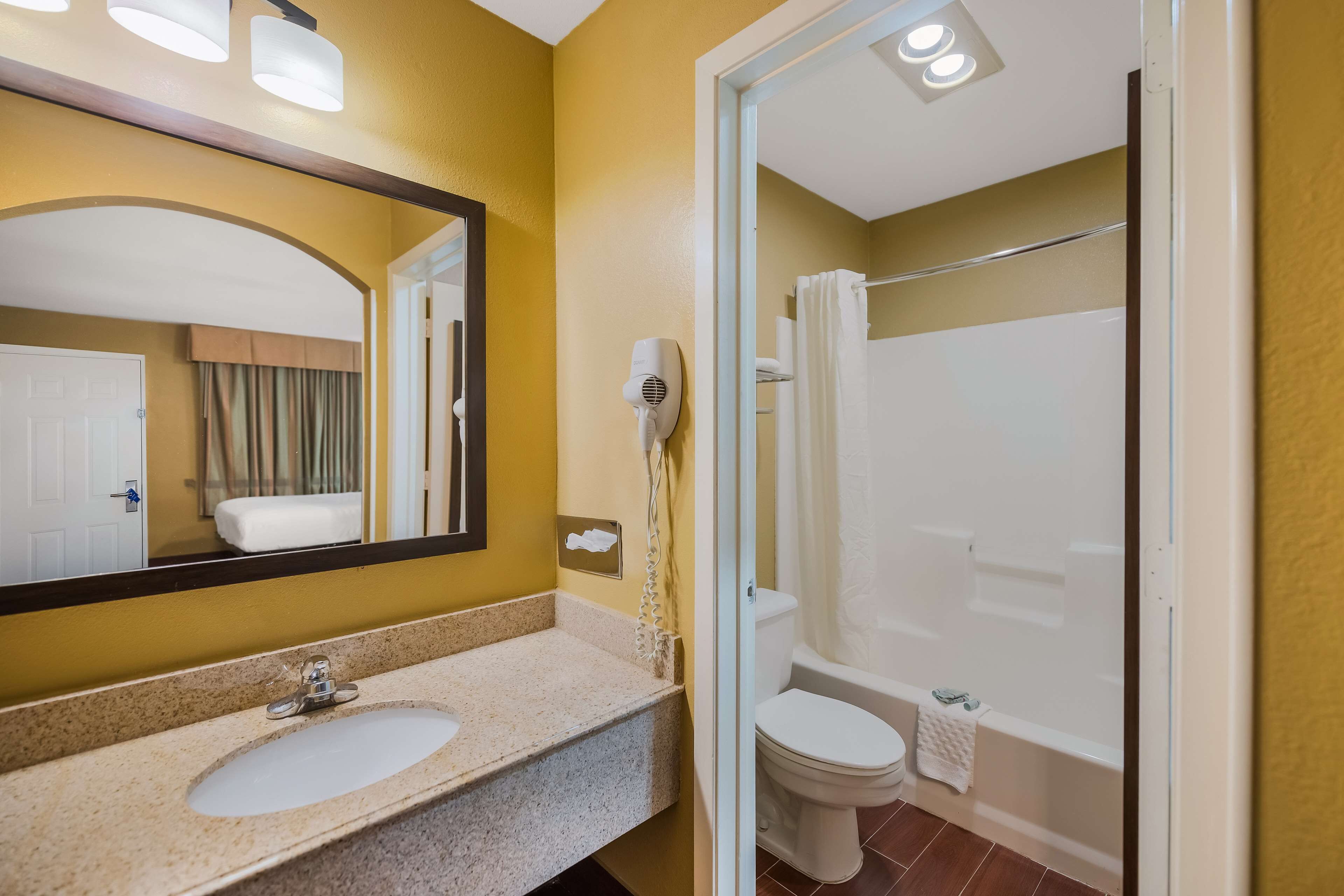 A bathroom with a sink, mirror, hairdryer, and a shower area.