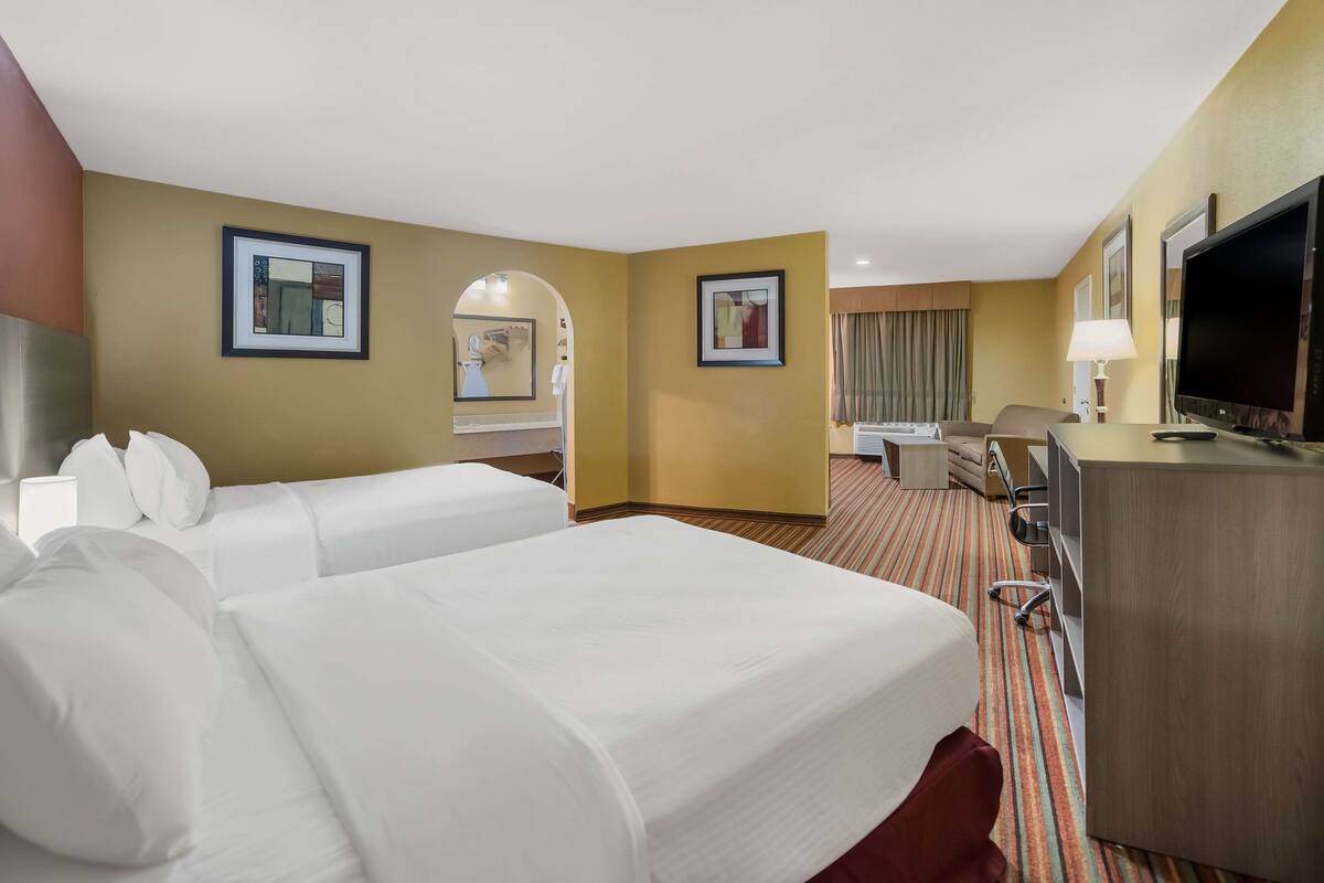A hotel room with two beds, a desk, a television, and a bathroom visible through an archway.