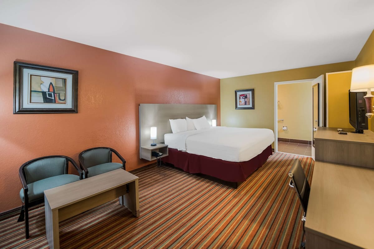 A hotel room with a bed, two chairs, a desk, a nightstand, and a mirror.
