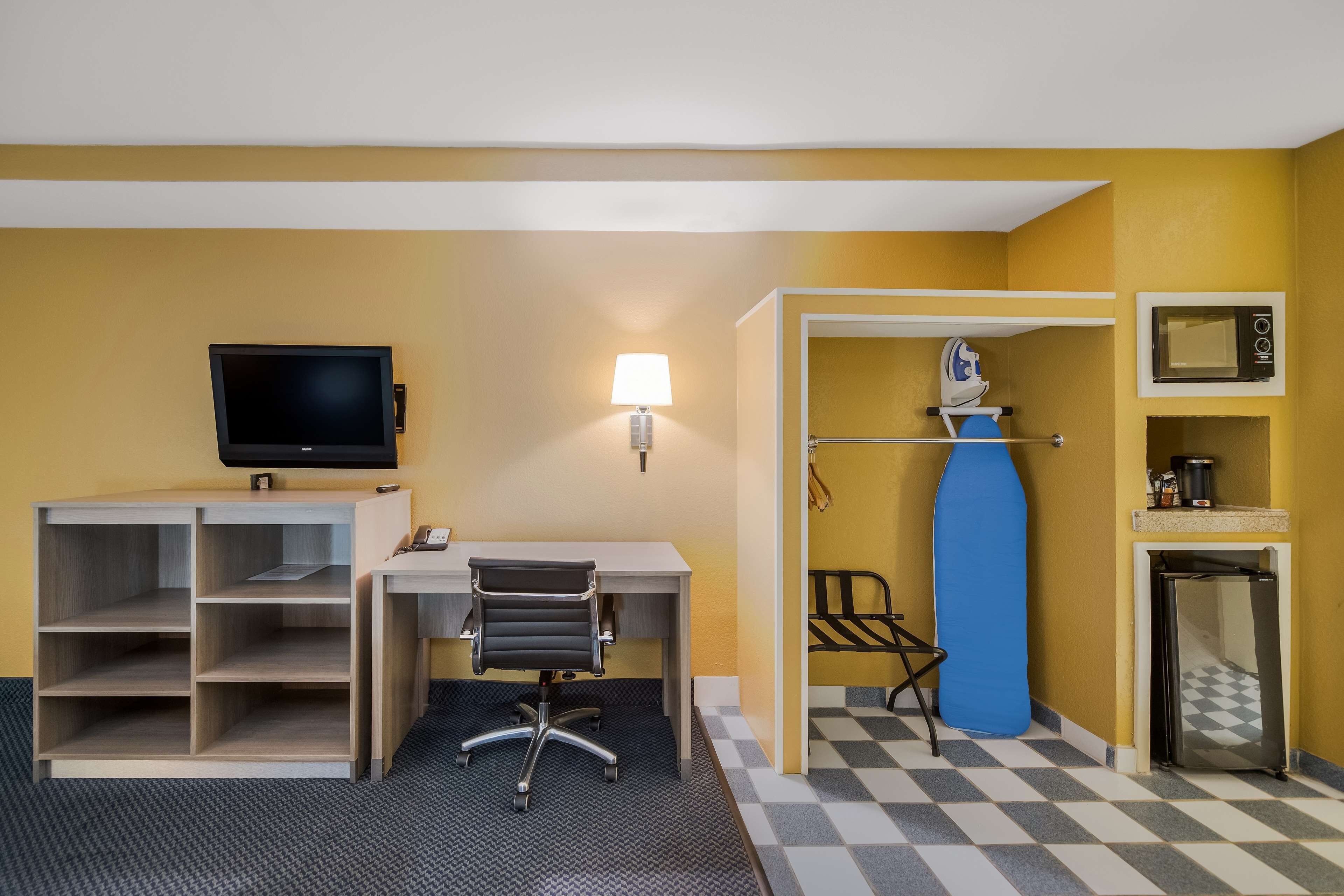 A hotel room with a desk, chair, TV, lamp, microwave, and mini-fridge.