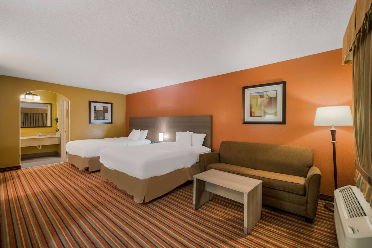 A hotel room with a double bed, a sofa, a small table, a lamp, and a picture on the wall.