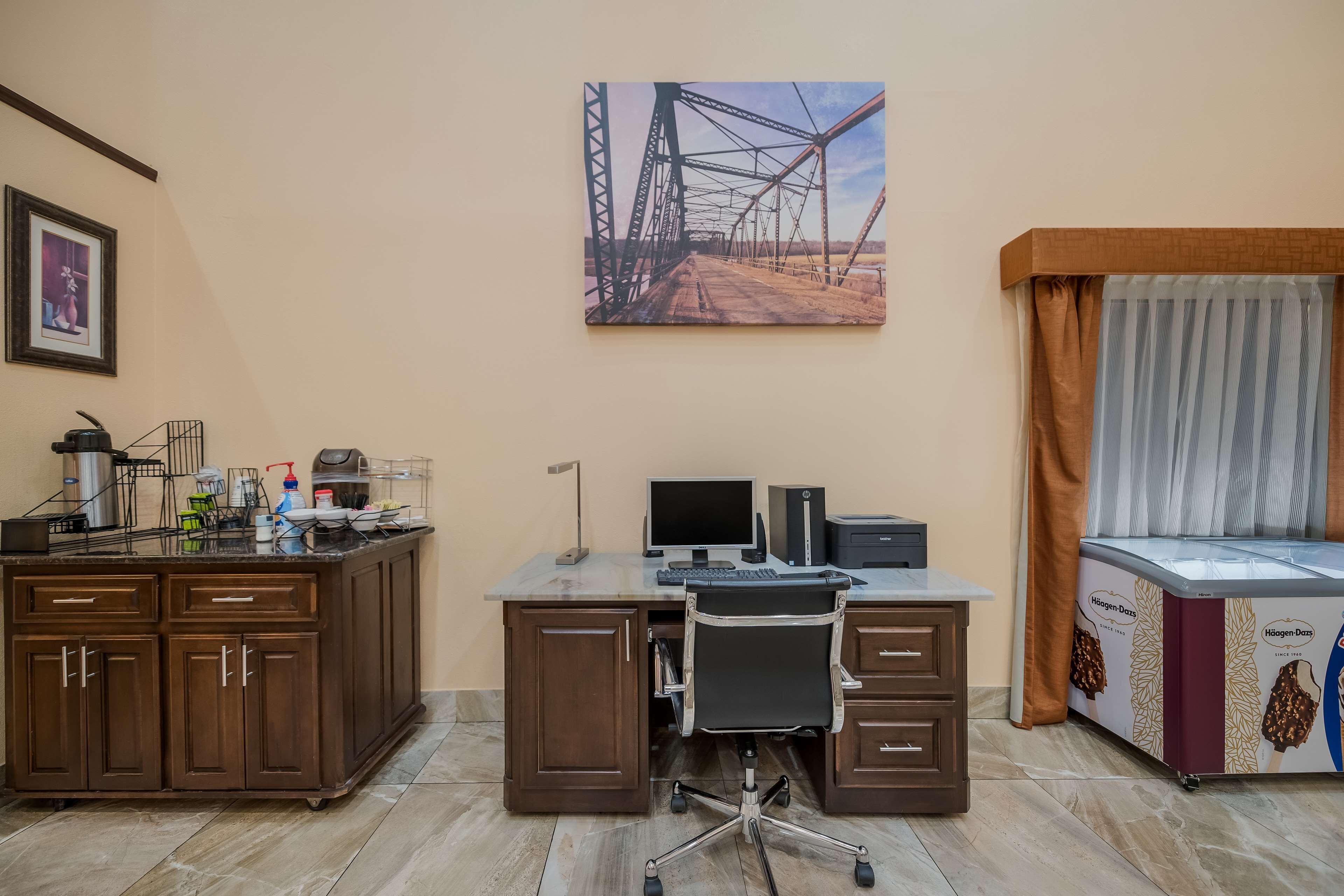 A modern office with a desk, computer, and office chair. There is a painting on the wall and a window with curtains.
