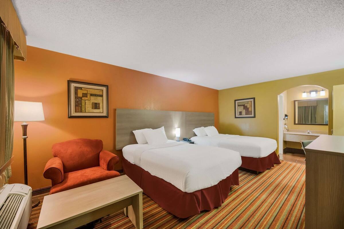 A hotel room with two beds, a desk, a chair, a lamp, and a mirror.