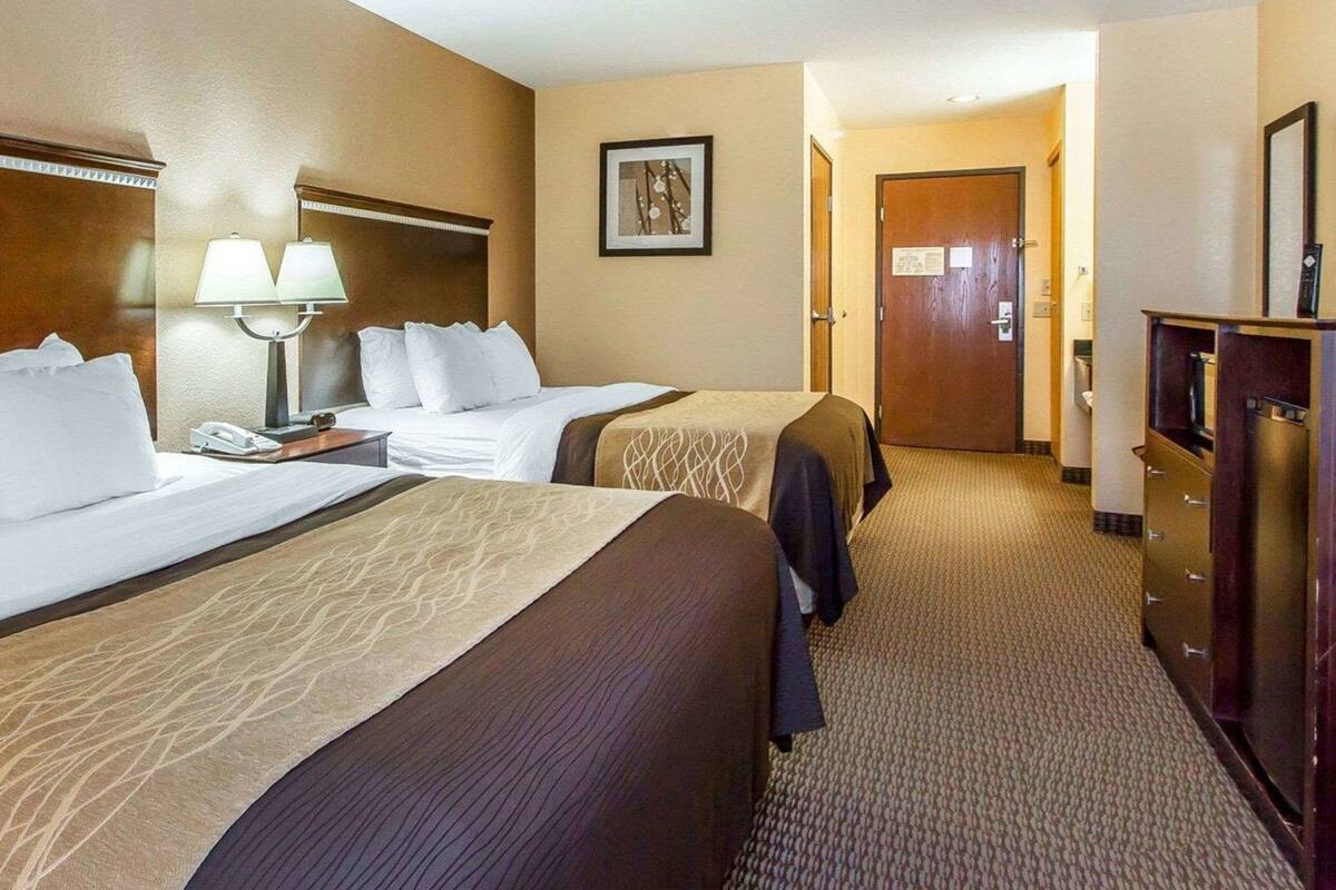 A hotel room with two beds, a desk with a lamp, a dresser, and a framed picture on the wall.