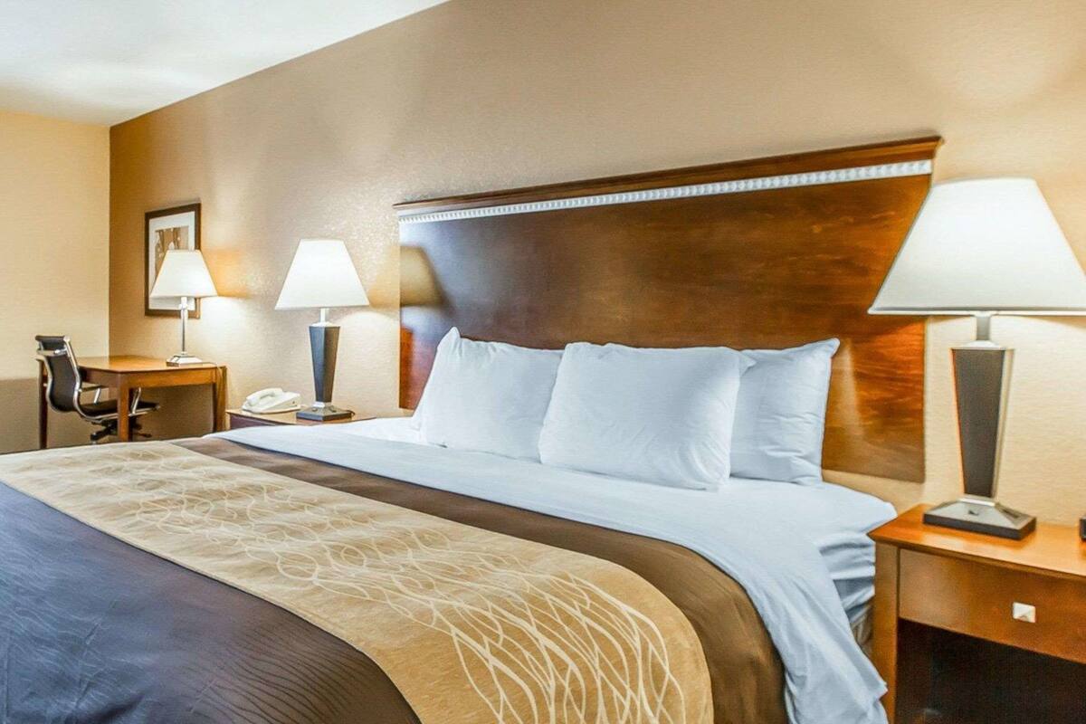 Une chambre d’hôtel avec un grand lit, deux tables de chevet avec des lampes, un bureau avec une chaise et un tableau encadré au mur.