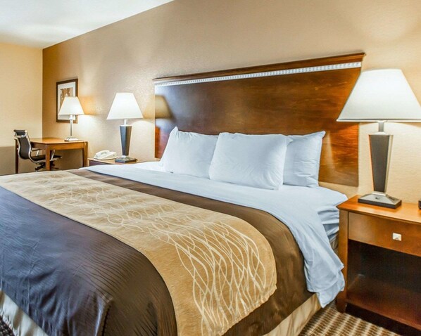 A hotel room with a large bed, two bedside tables with lamps, a desk with a chair, and a framed picture on the wall.