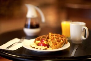 A breakfast setting with waffles, fruit, and a coffee cup on a table.