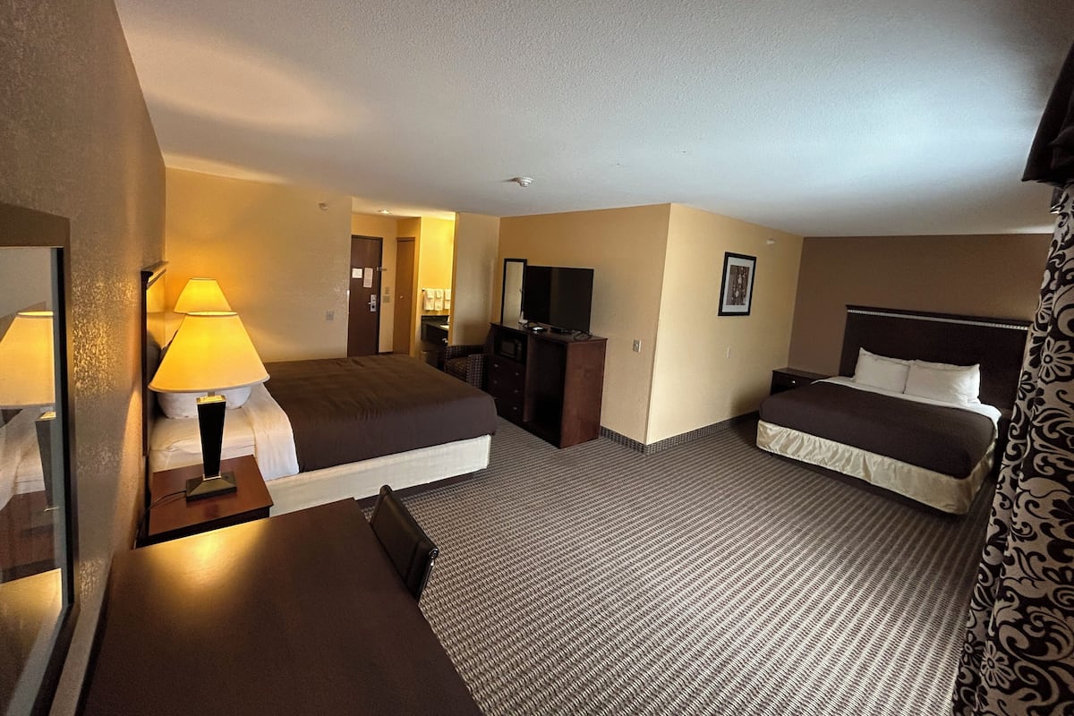 Une chambre d’hôtel avec deux lits, un bureau, une chaise, une commode, un miroir, une lampe et un téléviseur.