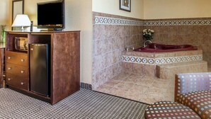 A bathroom with a marble-tiled wall, a large bathtub, a wooden vanity with a television, and a patterned rug.