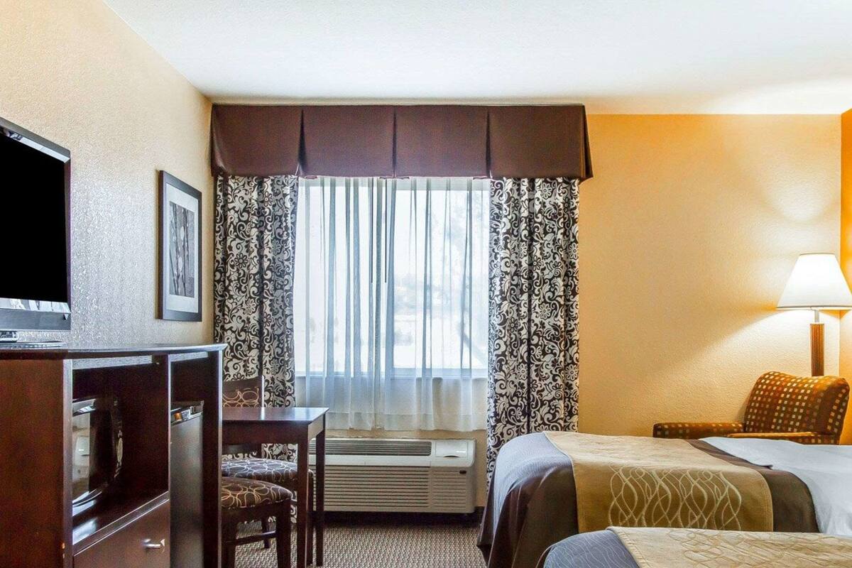 Une chambre d’hôtel avec un lit, un bureau, une télévision et une fenêtre avec des rideaux.