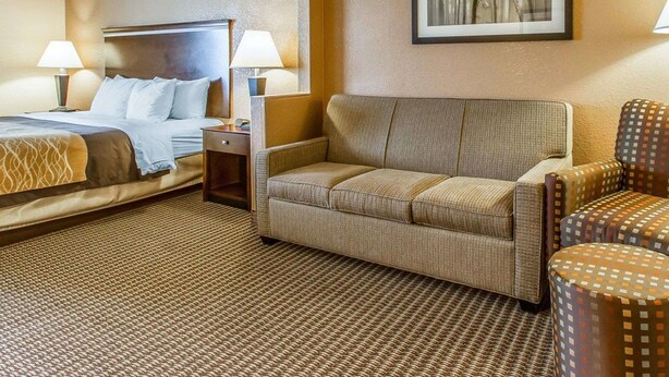 A hotel room with a bed, a sofa, a chair, and a nightstand with lamps.
