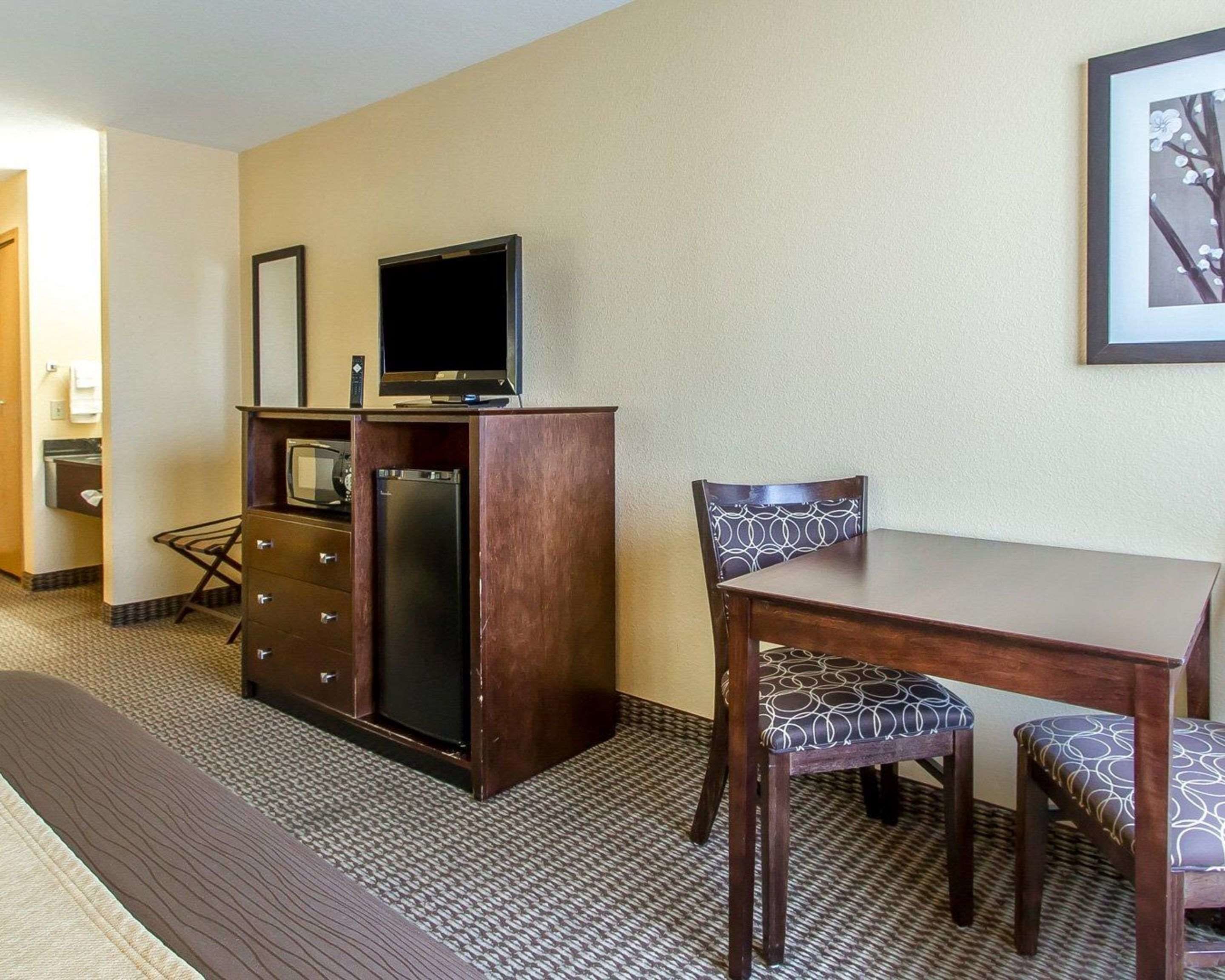 A hotel room with a wooden desk, two chairs, a television on a cabinet, and a framed picture on the wall.