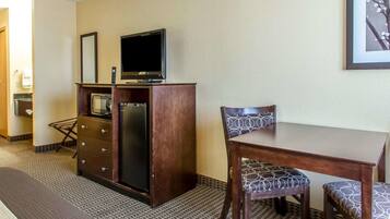 A hotel room with a wooden desk, two chairs, a television on a cabinet, and a framed picture on the wall.