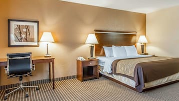 Une chambre d’hôtel comprenant un lit, deux tables de chevet avec des lampes, un bureau avec une chaise et un tableau encadré au mur.