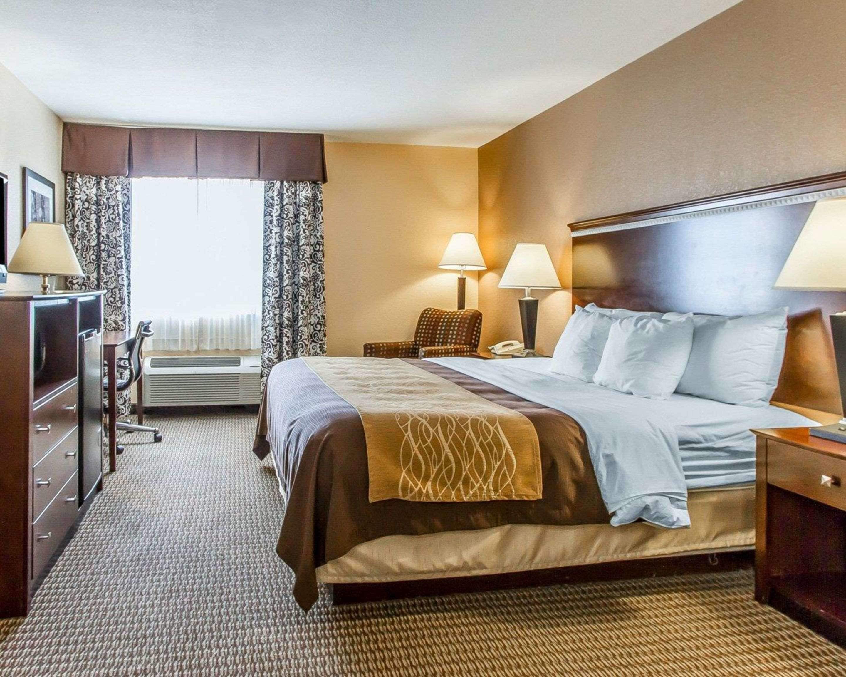 A hotel room with a large bed, two bedside lamps, a chair, a desk, and a dresser.