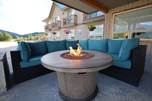 Ein runder Außenbereich mit Sitzgelegenheiten und einem Feuerkorb in der Mitte, umgeben von Türkis-Kissen auf einer Rattan-Couch.