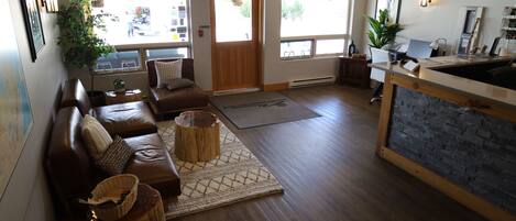 A spacious lobby with a brown leather sofa, a wooden reception desk, and large windows offering views of the outside.