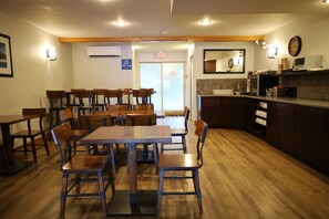 A dining area with wooden tables and chairs, a kitchen area with a microwave and sink, and an exit sign. - Glacier Mountain Lodge (Blue River)