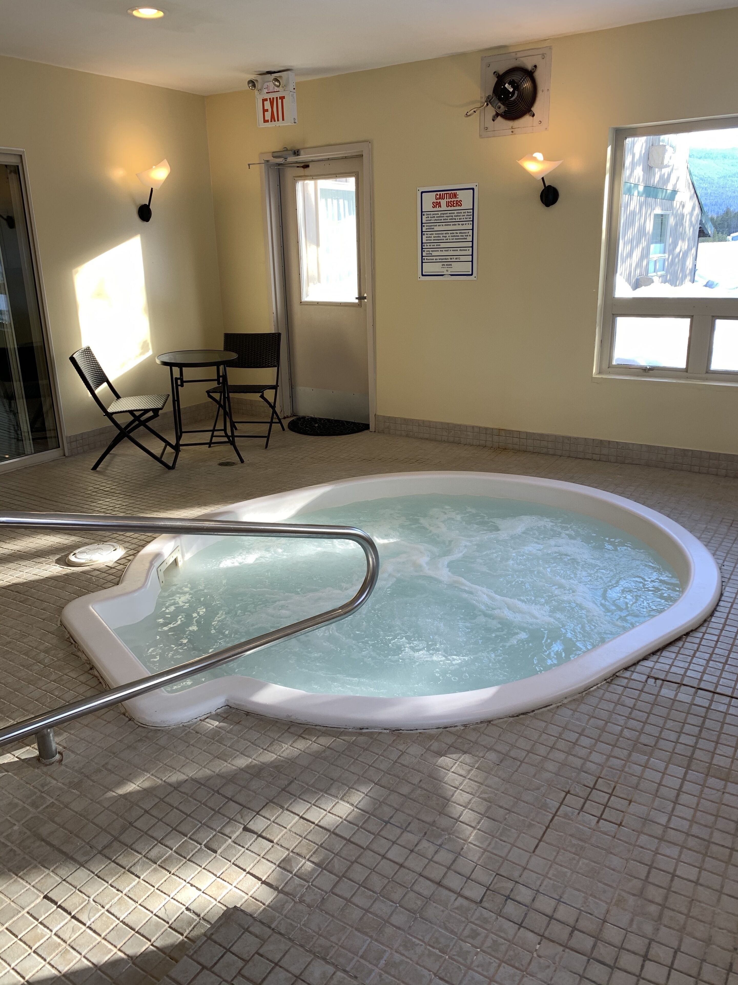 Una piscina interior amb un banyera d'hidromassatge, una taula amb cadires i vista cap a l'exterior.