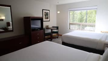 A hotel room with a bed, a desk with a chair, a television, a window with a view of trees, and a framed picture on the wall.