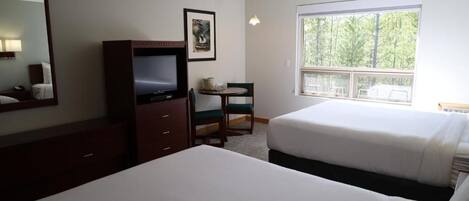 A hotel room with a bed, a desk with a chair, a television, a window with a view of trees, and a framed picture on the wall.