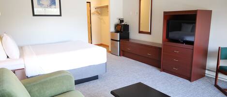 A hotel room with a bed, a green sofa, a wooden dresser, a television, and a microwave.