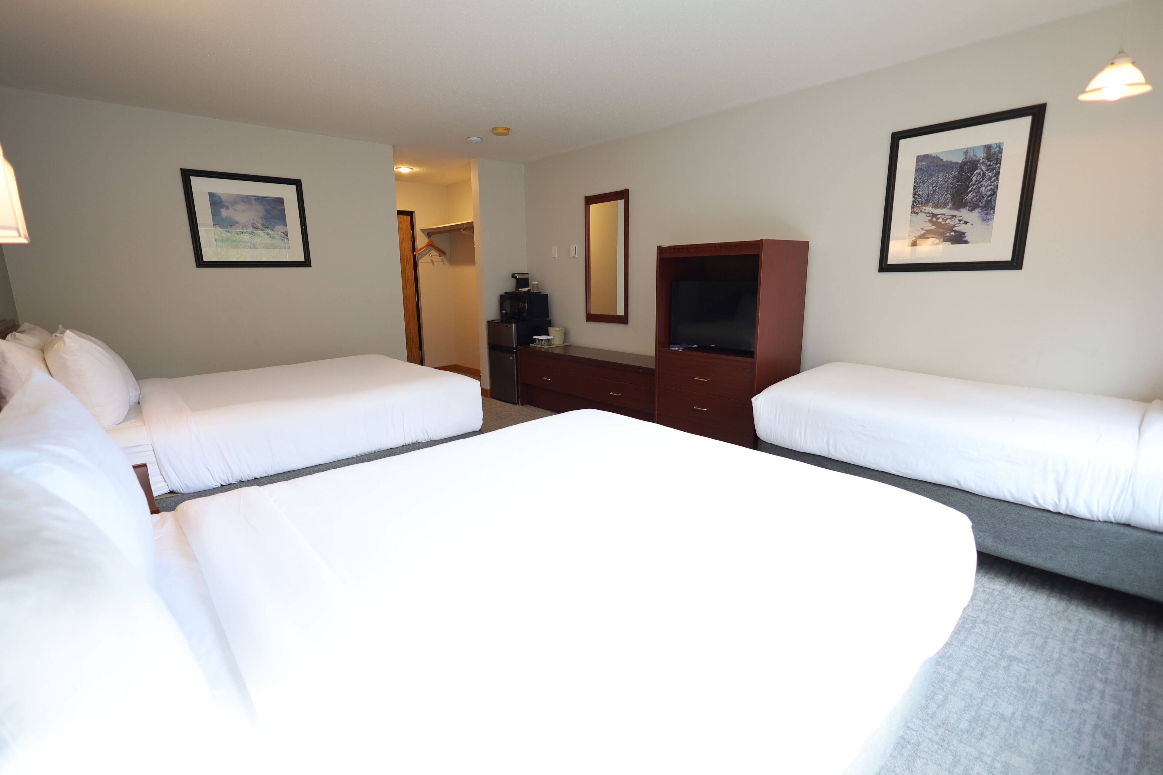 Une chambre d’hôtel avec deux lits simples, une commode, un téléviseur et des tableaux encadrés aux murs.