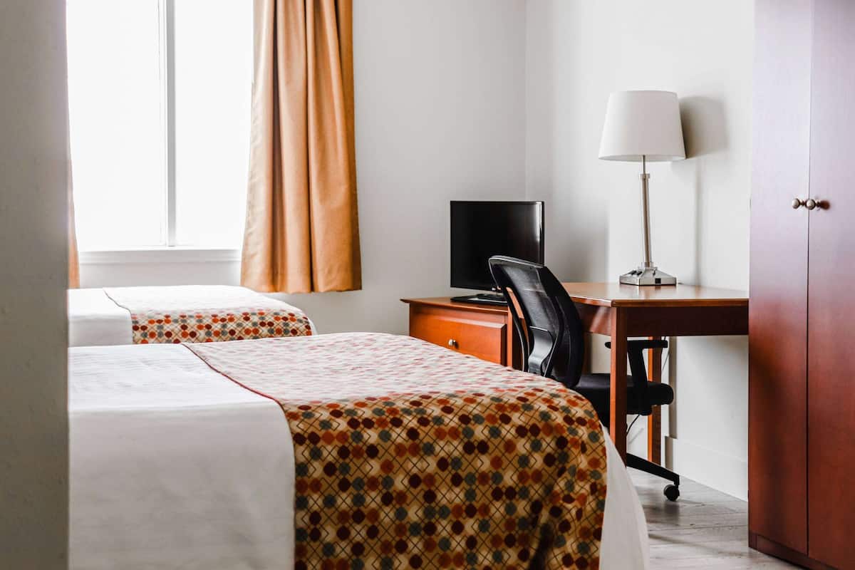A hotel room with two beds, a desk with a computer, a chair, and a lamp.