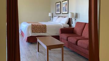A hotel room with a bed, a red sofa, a wooden table, and two wall-mounted lamps.