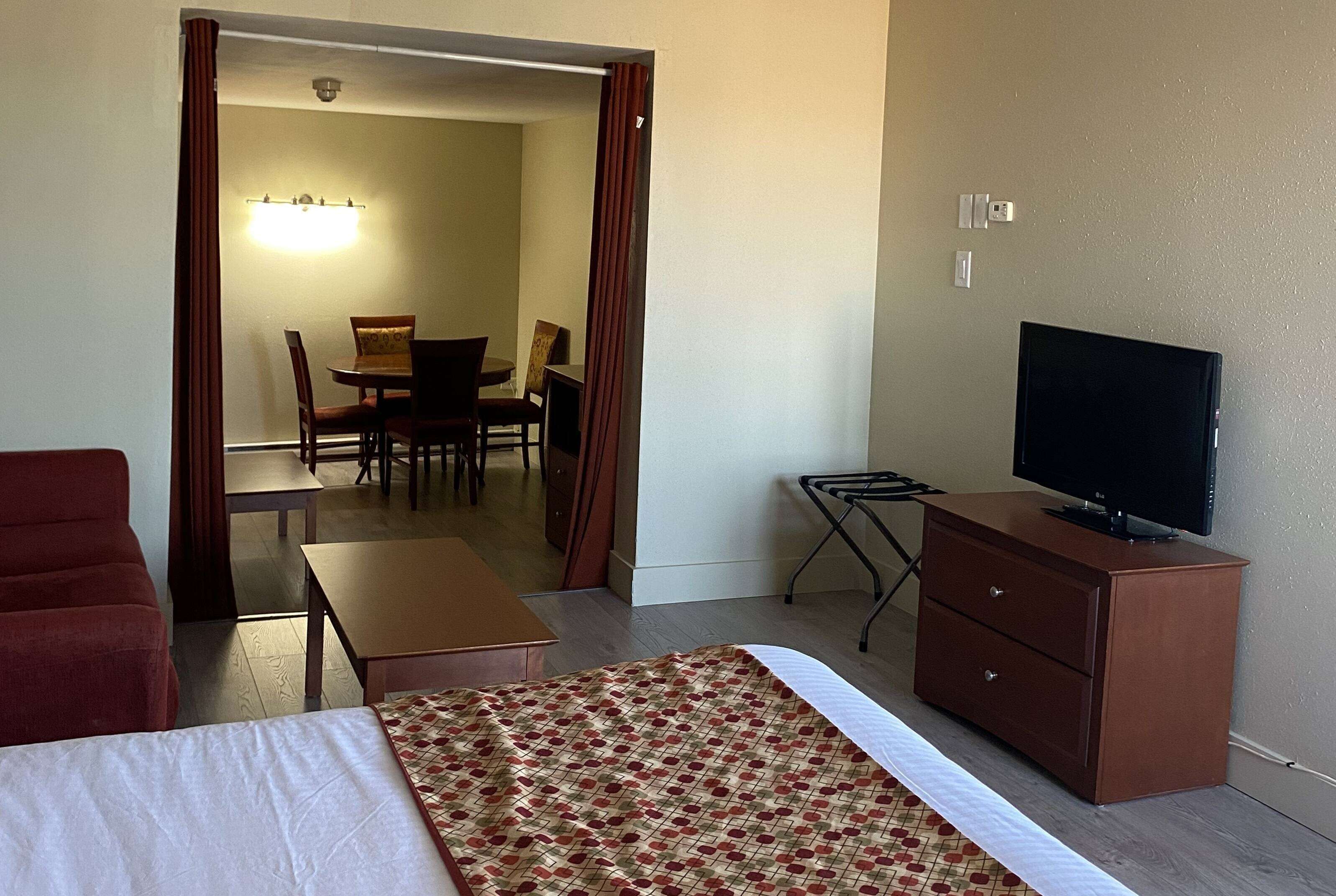 Una habitación de hotel con cama, televisión sobre un mueble de madera, escritorio y un área de comedor con sillas y una mesa.