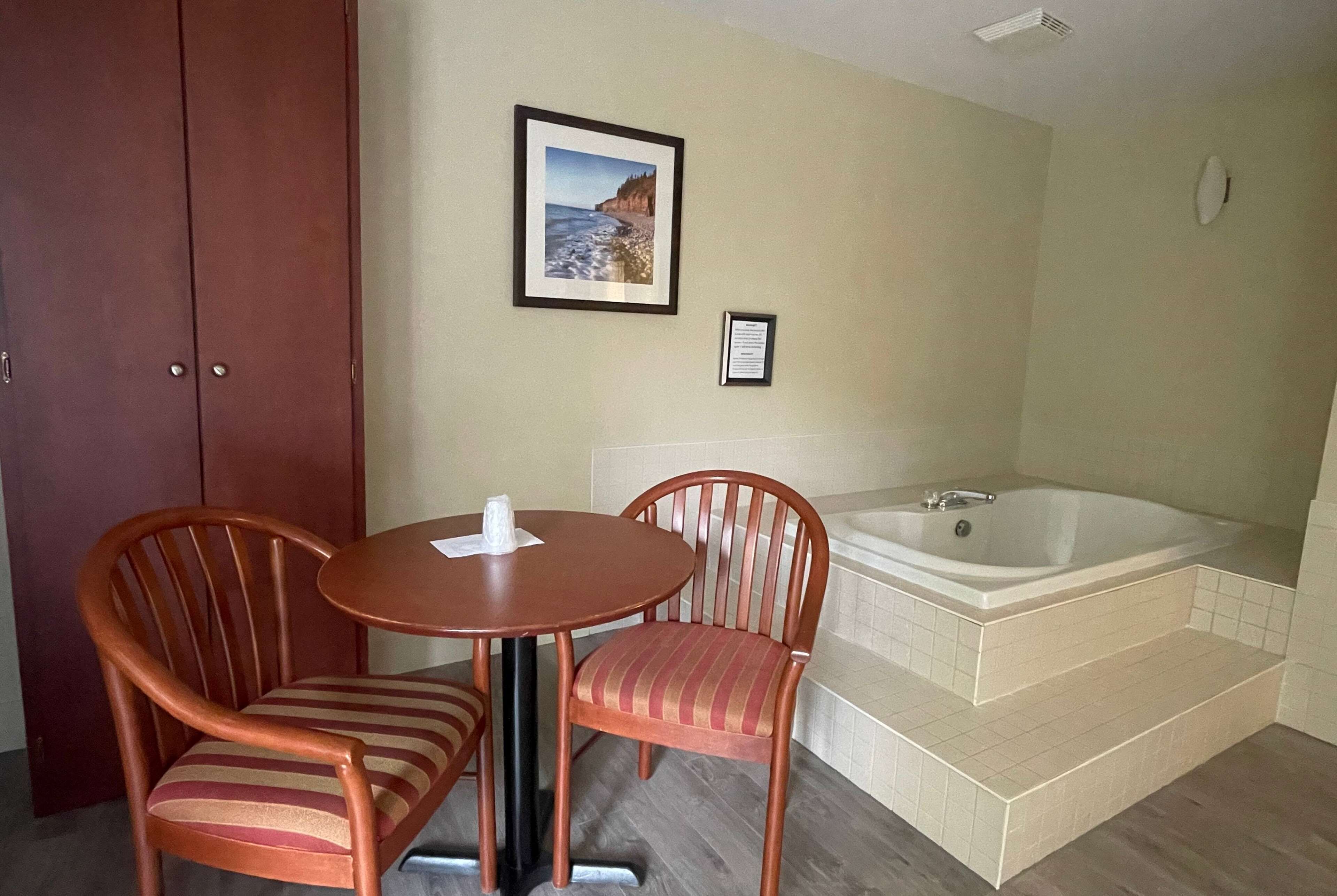 A room with a wooden table and two chairs, a framed picture on the wall, and a bathtub with steps.