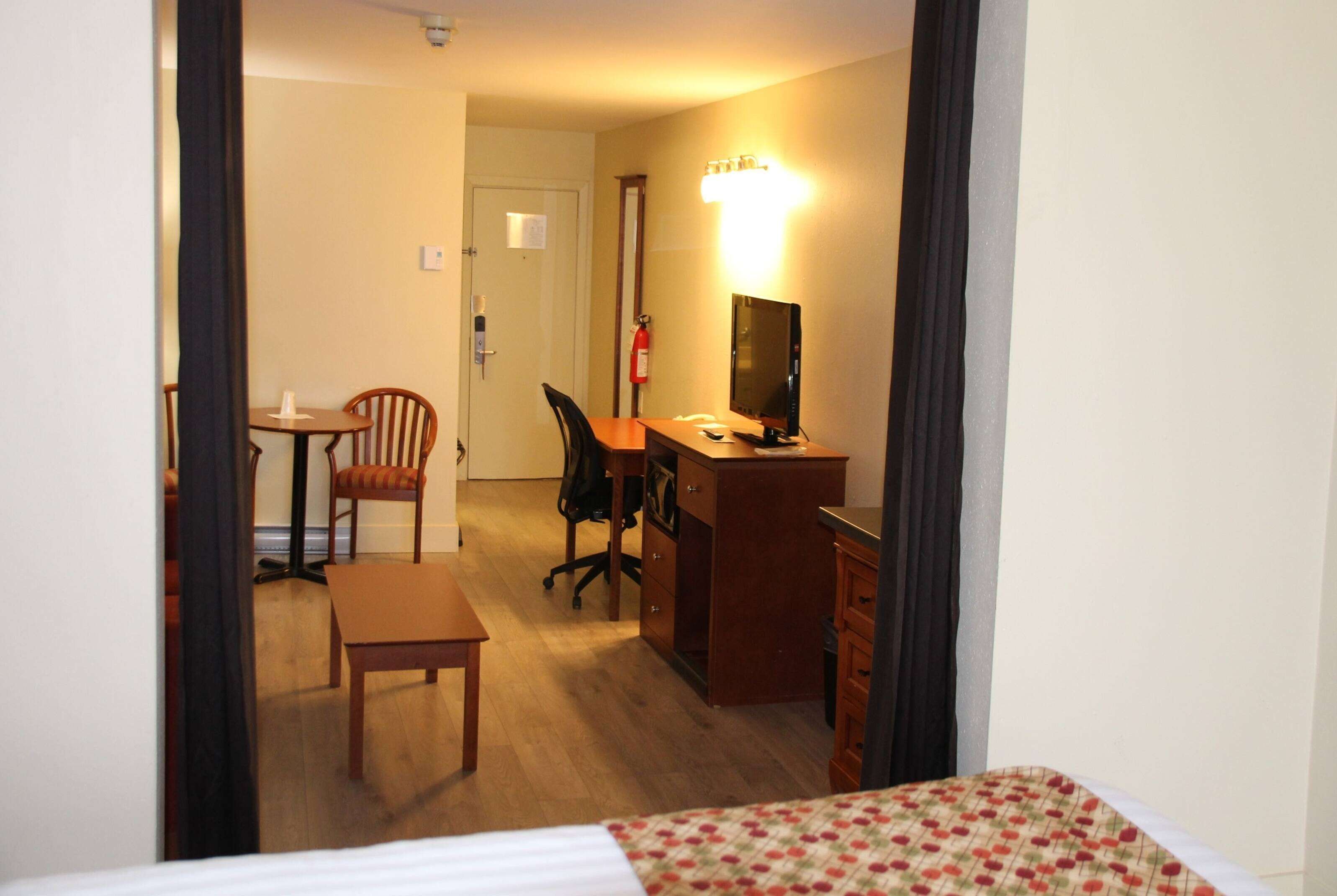 A hotel room with a bed, a desk with a computer, a chair, a small table, and a fire extinguisher.